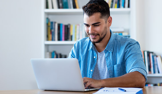 Photo of a man working on a computer with paper work near by